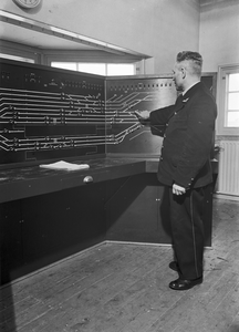 159671 Interieur van het seinhuis van de N.S. te 's-Hertogenbosch met de treindienstleider achter het NX-bedieningstableau.